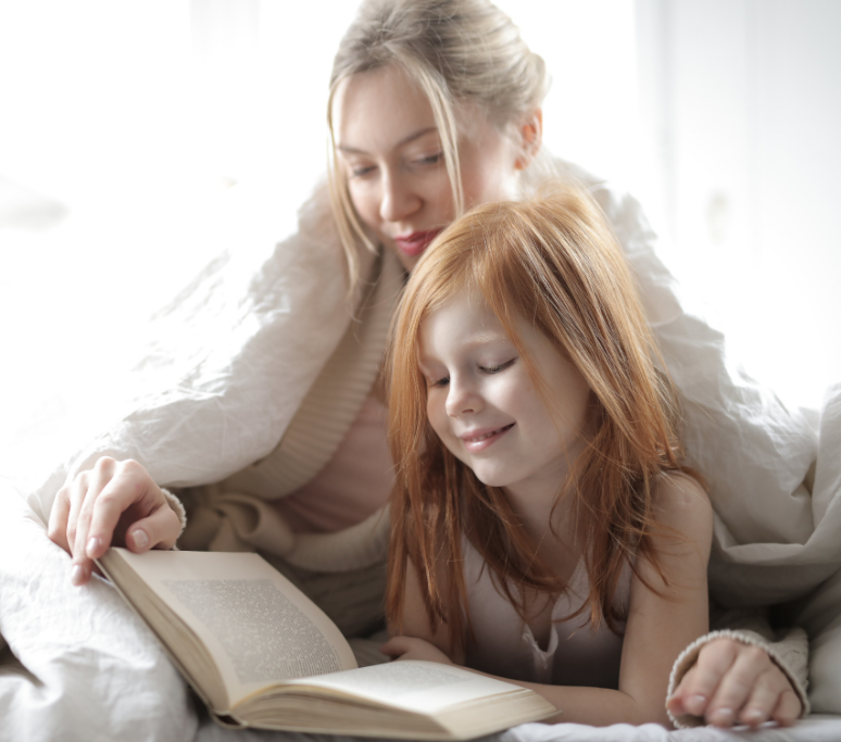 woman and young girl reading under a blanket